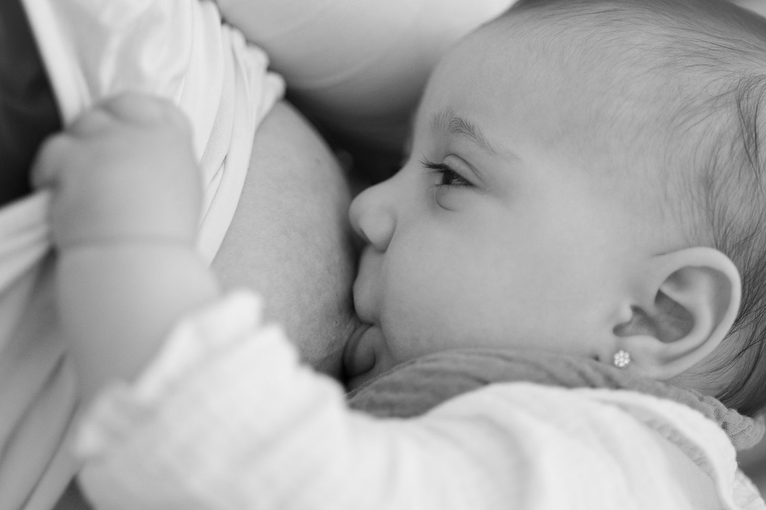 Intimate black and white image of infant nursing in natural light.