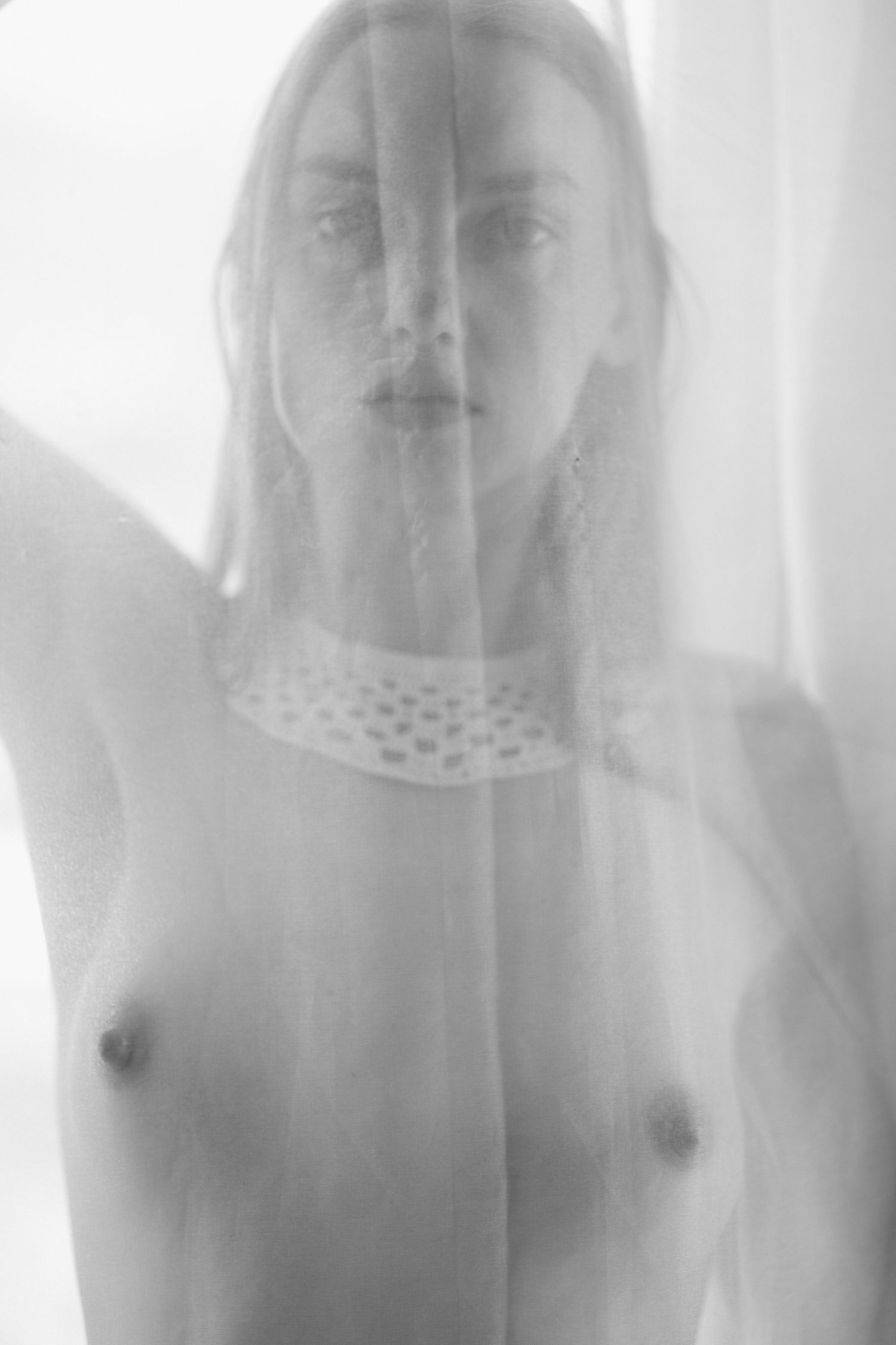 Artistic black and white portrait through sheer fabric creating a dreamy ethereal effect.