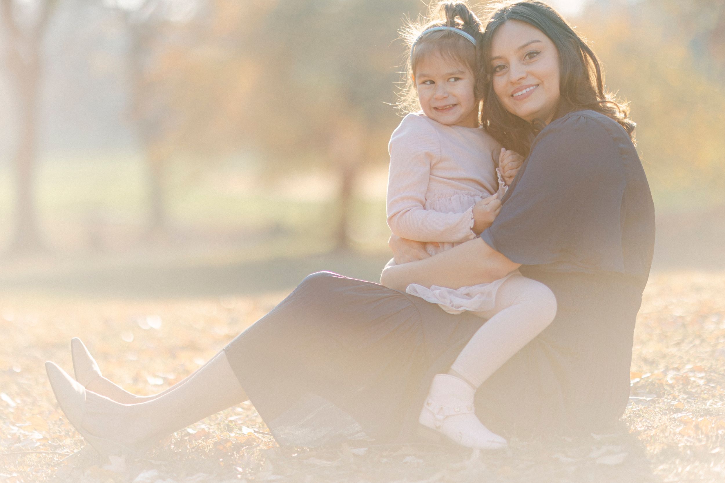 Parent and child sit together on ground during golden hour outdoor portrait session.