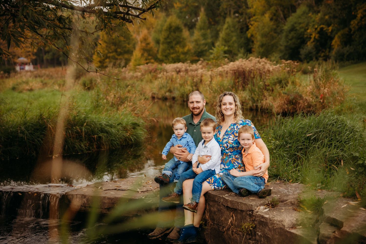 Family sitting together on rocks by a peaceful stream in nature.
