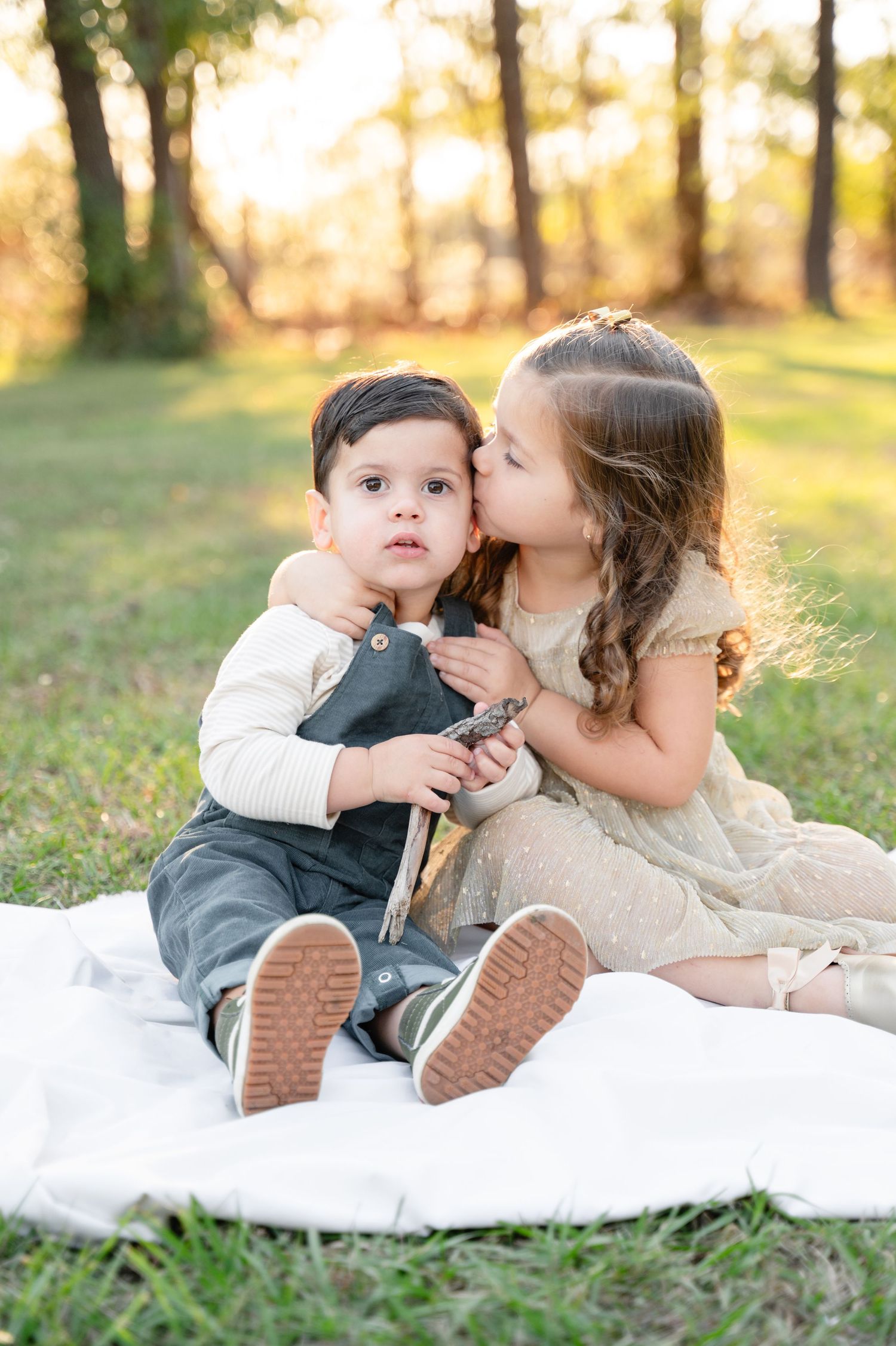A happy family of three posing together outdoors with trees in the background.