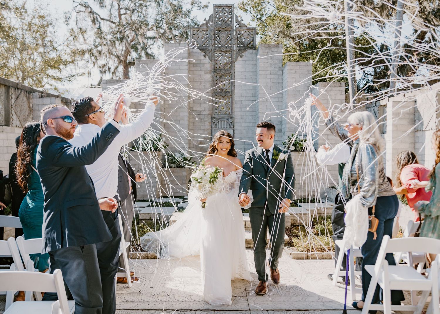 Jenna & Nelson smiling as they exit the aisle at Maitland Art & History Center wedding chapel, with white streamers. Cred: LexTakePix