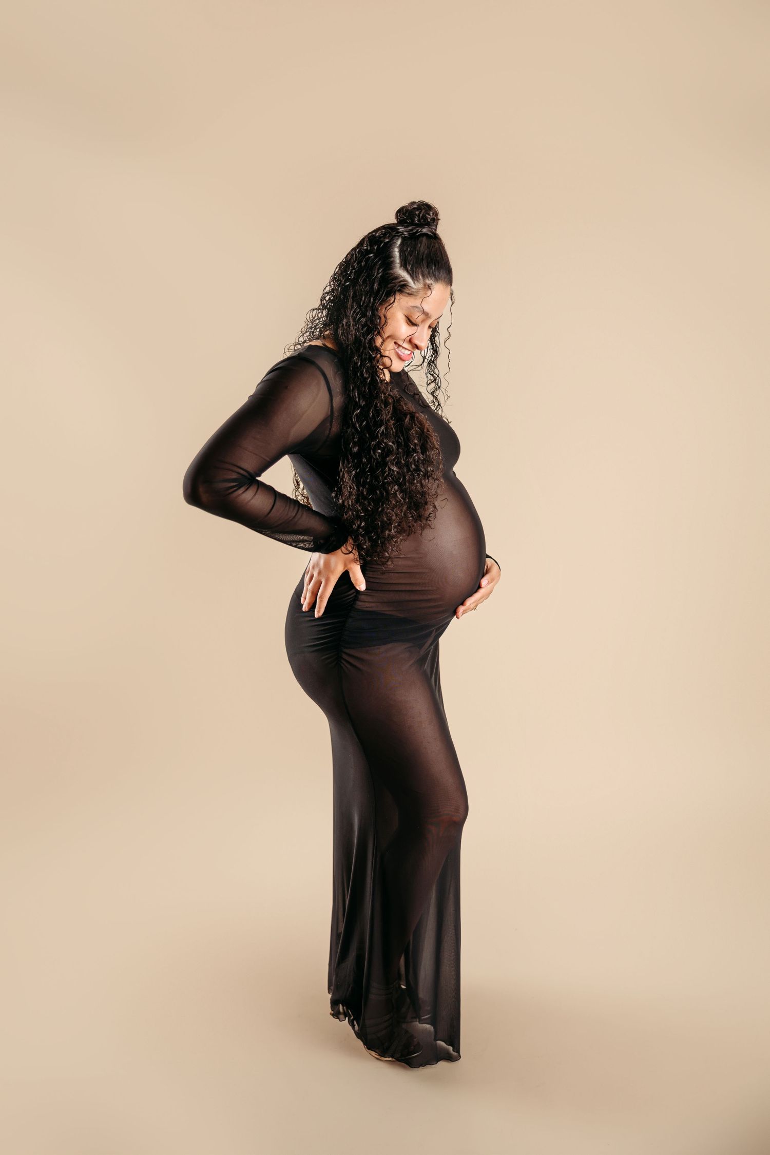 A maternity photo showing a pregnant woman in a black dress posing against a neutral backdrop.Middle Tennessee Luxury Maternity Photographer