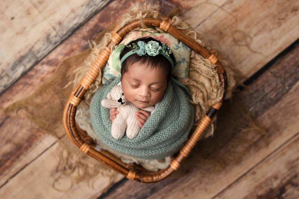 Sleeping newborn wrapped in mint green swaddle nestled in rustic basket on wooden background.