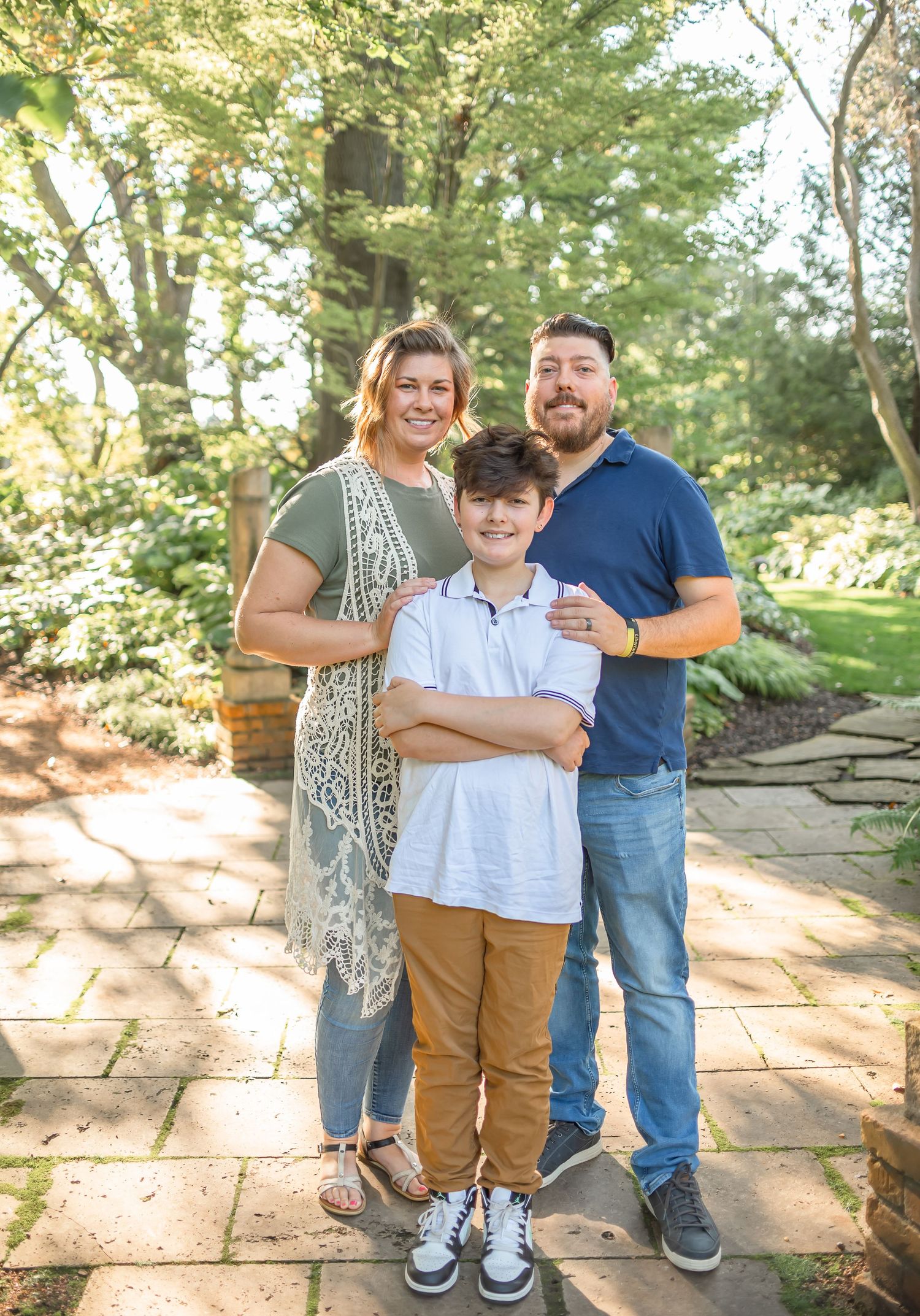 A family of three poses together on stone pavers in a garden setting.