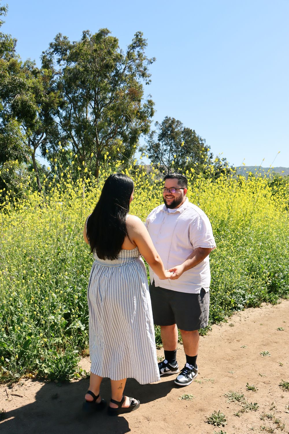 Couple standing on trail surrounded by yellow wildflowers on sunny day.