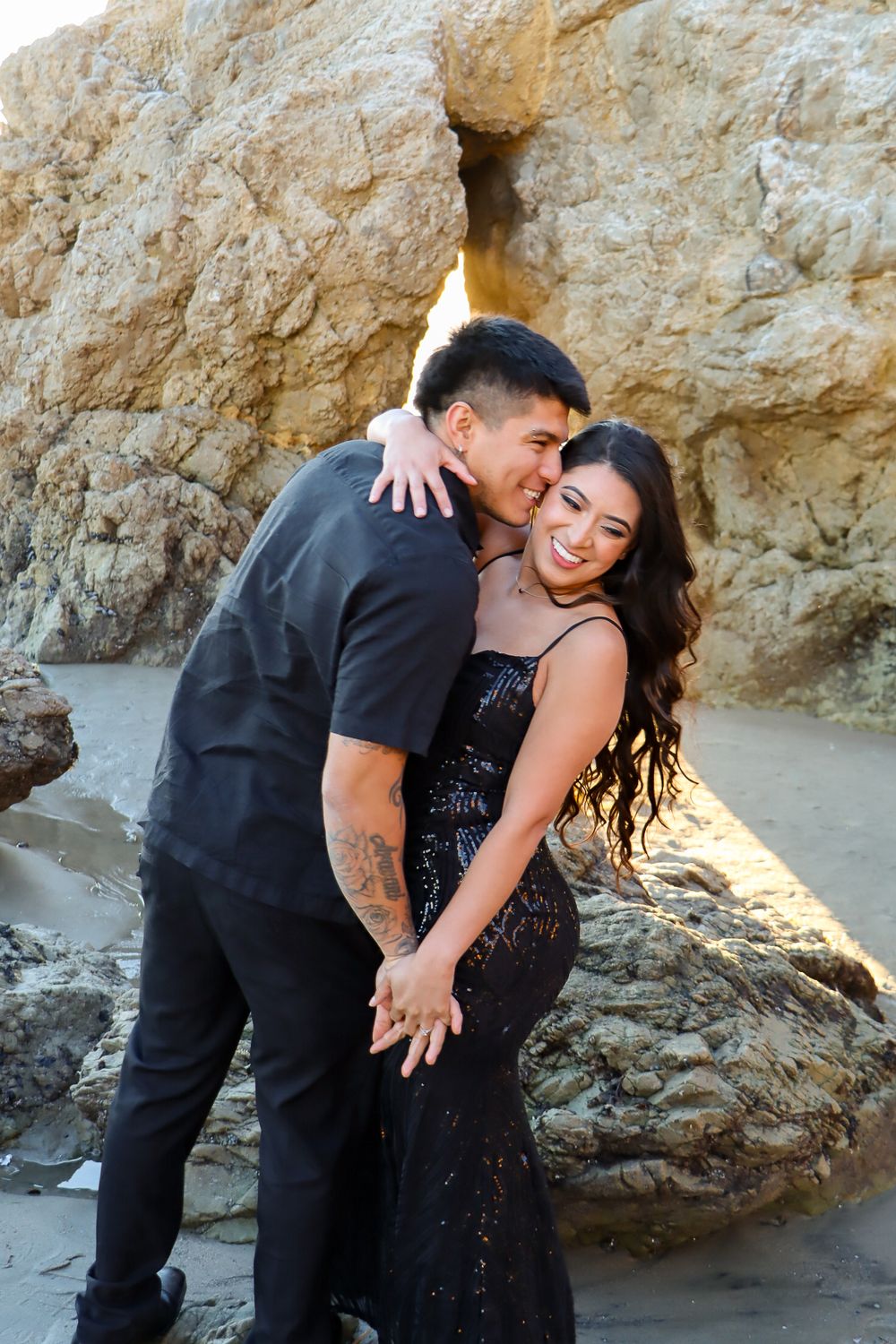 Couple shares joyful embrace during beach photoshoot near rocky cliffs.