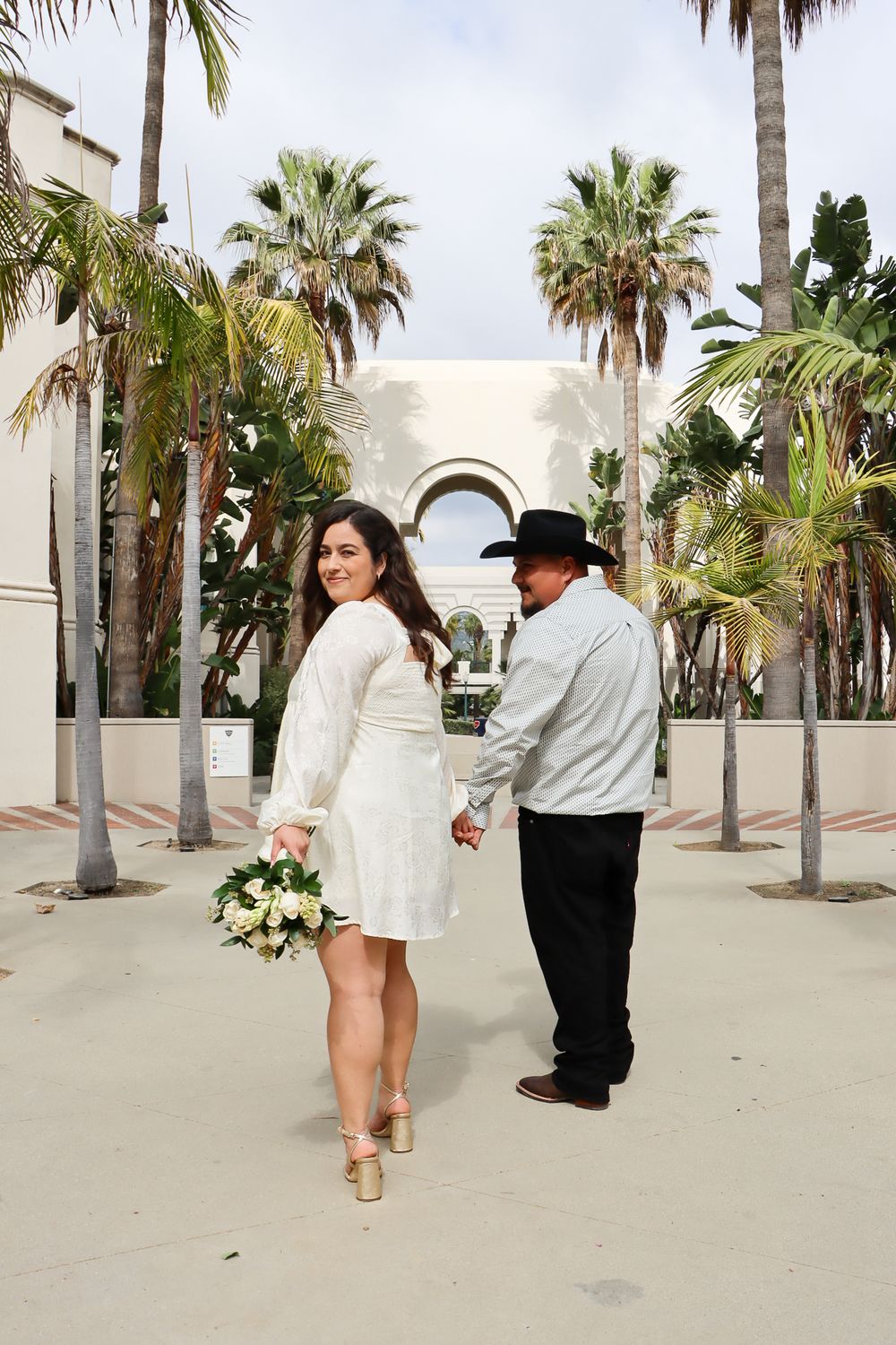 Couple poses together along a palm tree-lined walkway in a romantic photoshoot sequence.