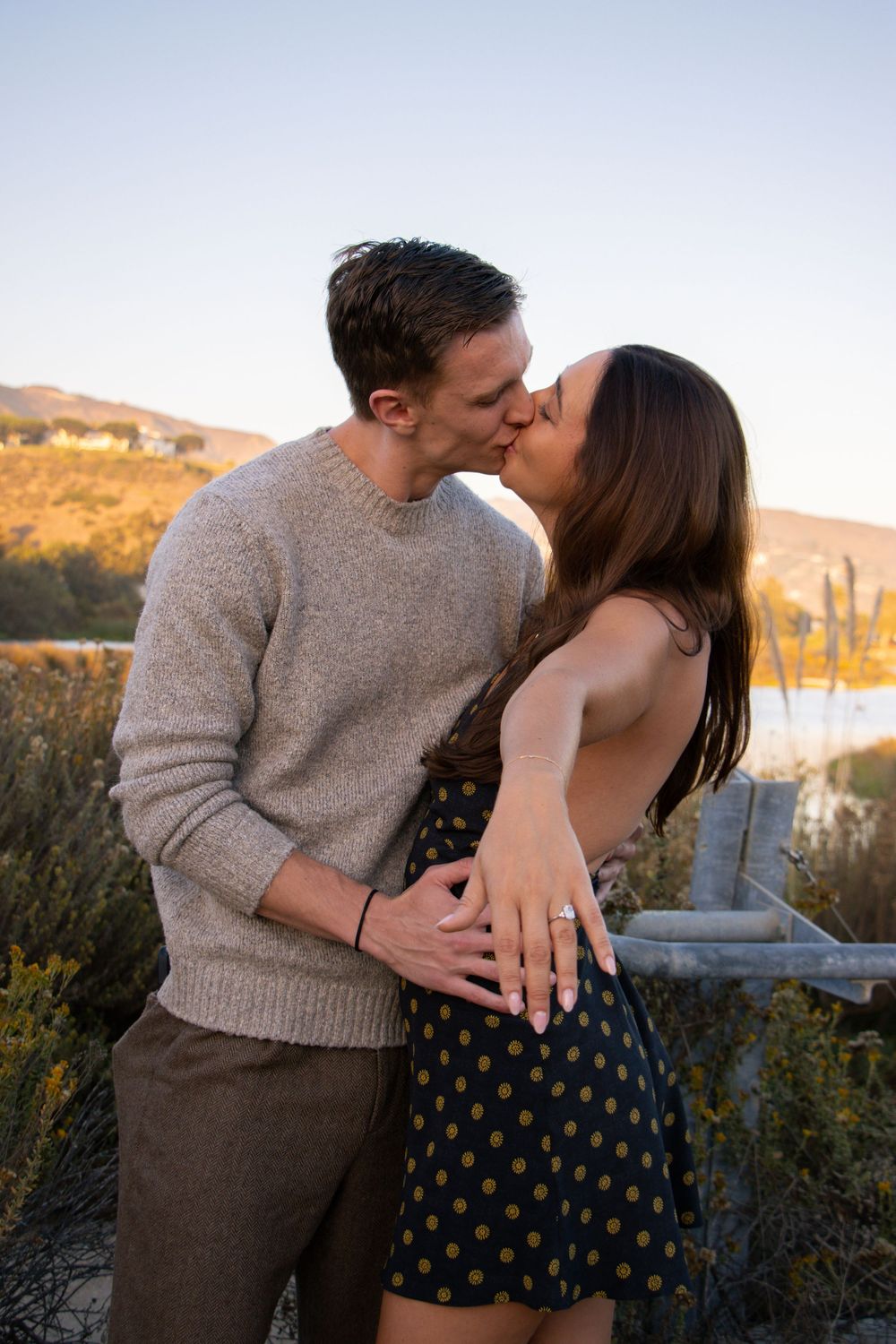 Romantic couple sharing a kiss at sunset with mountains in the background.