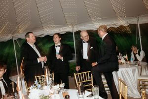 Four men in tuxedos socializing under a white tent at an elegant wedding reception.