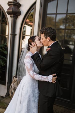 Bride and groom sharing romantic first kiss outside elegant venue with arched black doors.