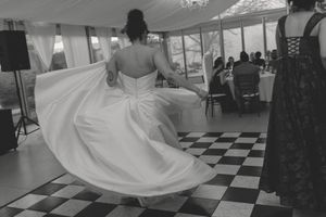 Bride twirling in white wedding gown on checkered dance floor in black and white wedding reception photo.