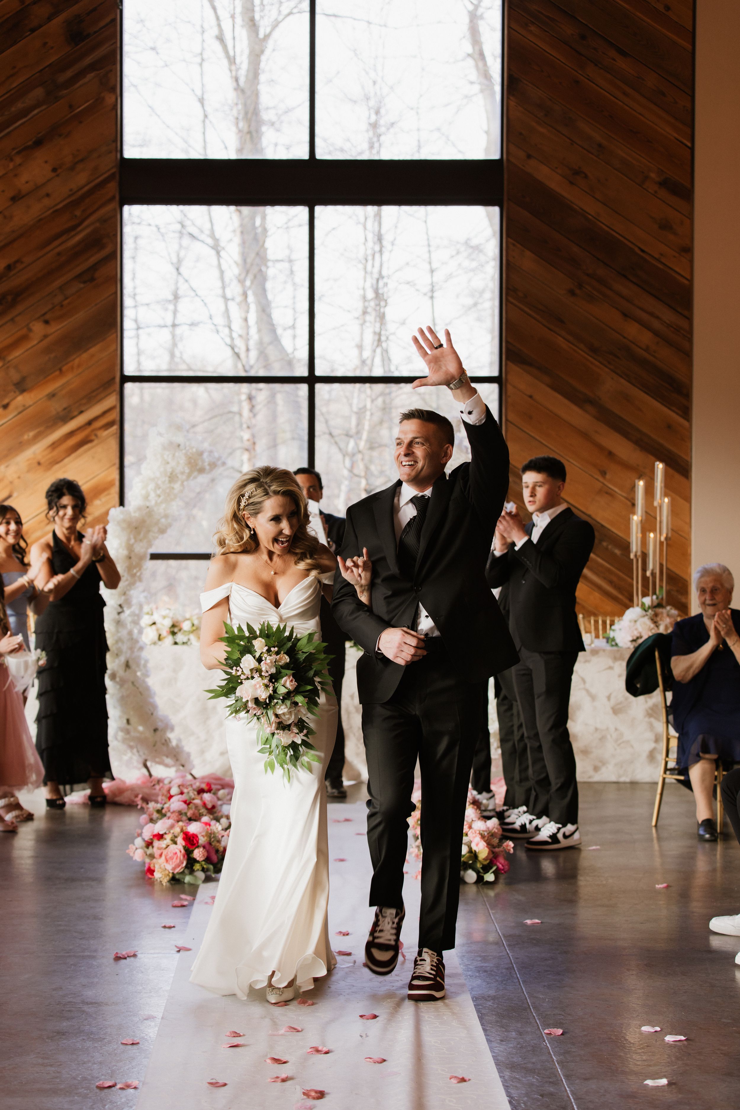 Newlyweds joyfully walk down the aisle after their ceremony in a rustic wood-paneled wedding venue.