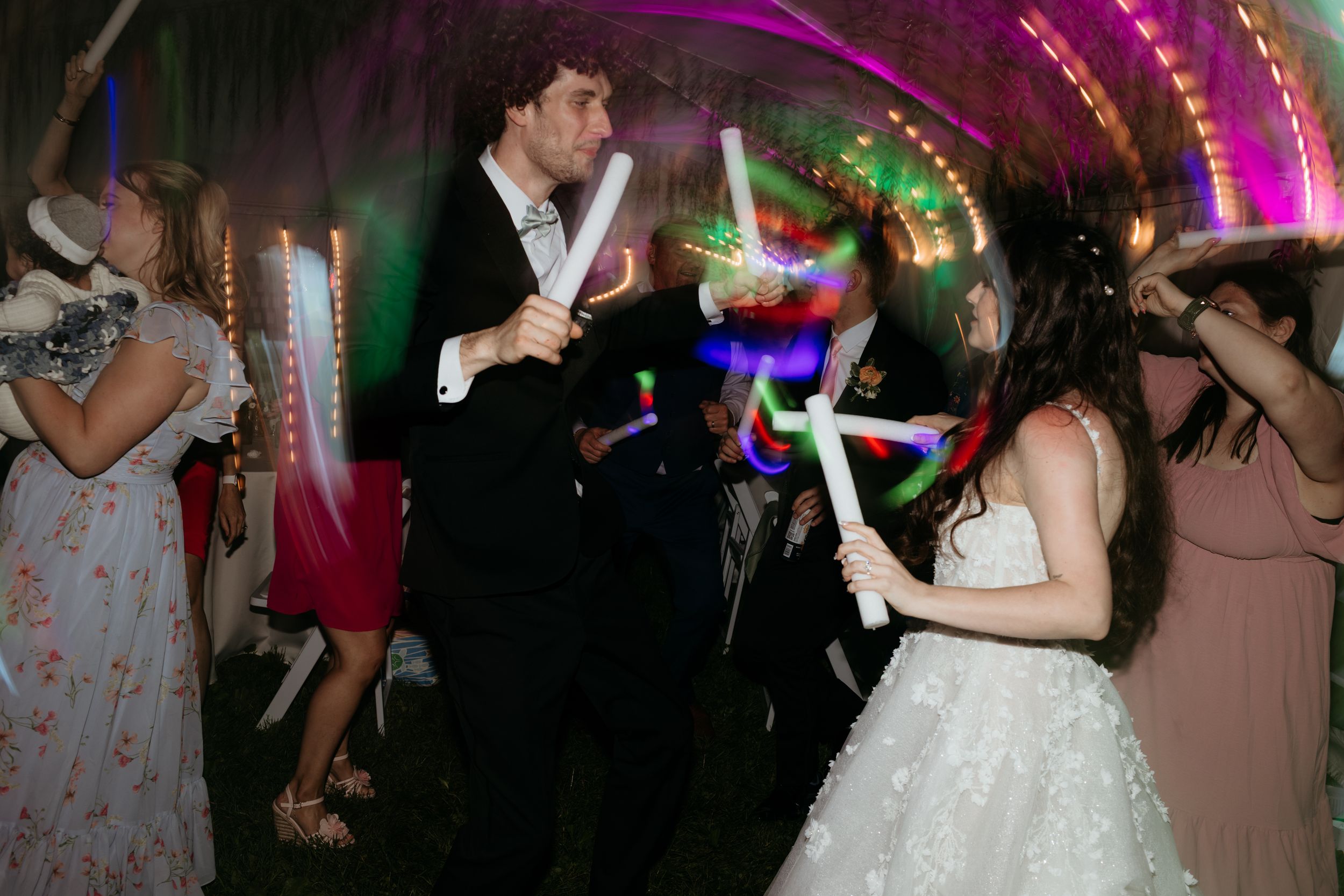 Bride and groom dancing with glowing wands at a colorful wedding reception party.
