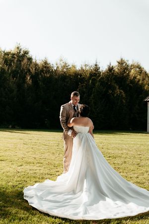 Bride in strapless ball gown with long train faces groom in tan suit on sunny green lawn.