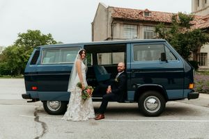 Bride and groom posing beside a vintage blue Volkswagen van on their wedding day.
