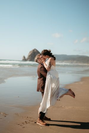 Groom lifts bride in a romantic embrace on the beach near Haystack Rock Oregon.