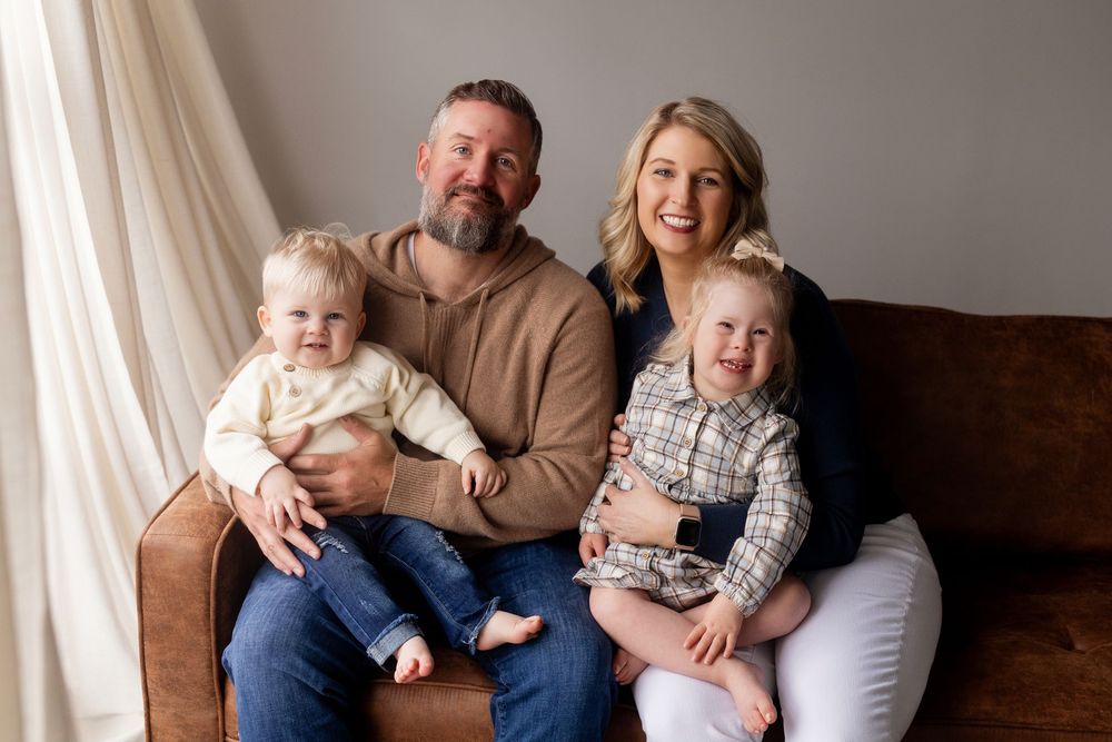 Family lounging together on brown leather couch in cozy home studio setting.