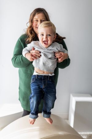A small child in jeans and gray sweater being lifted up and down in a playful sequence against a white background.