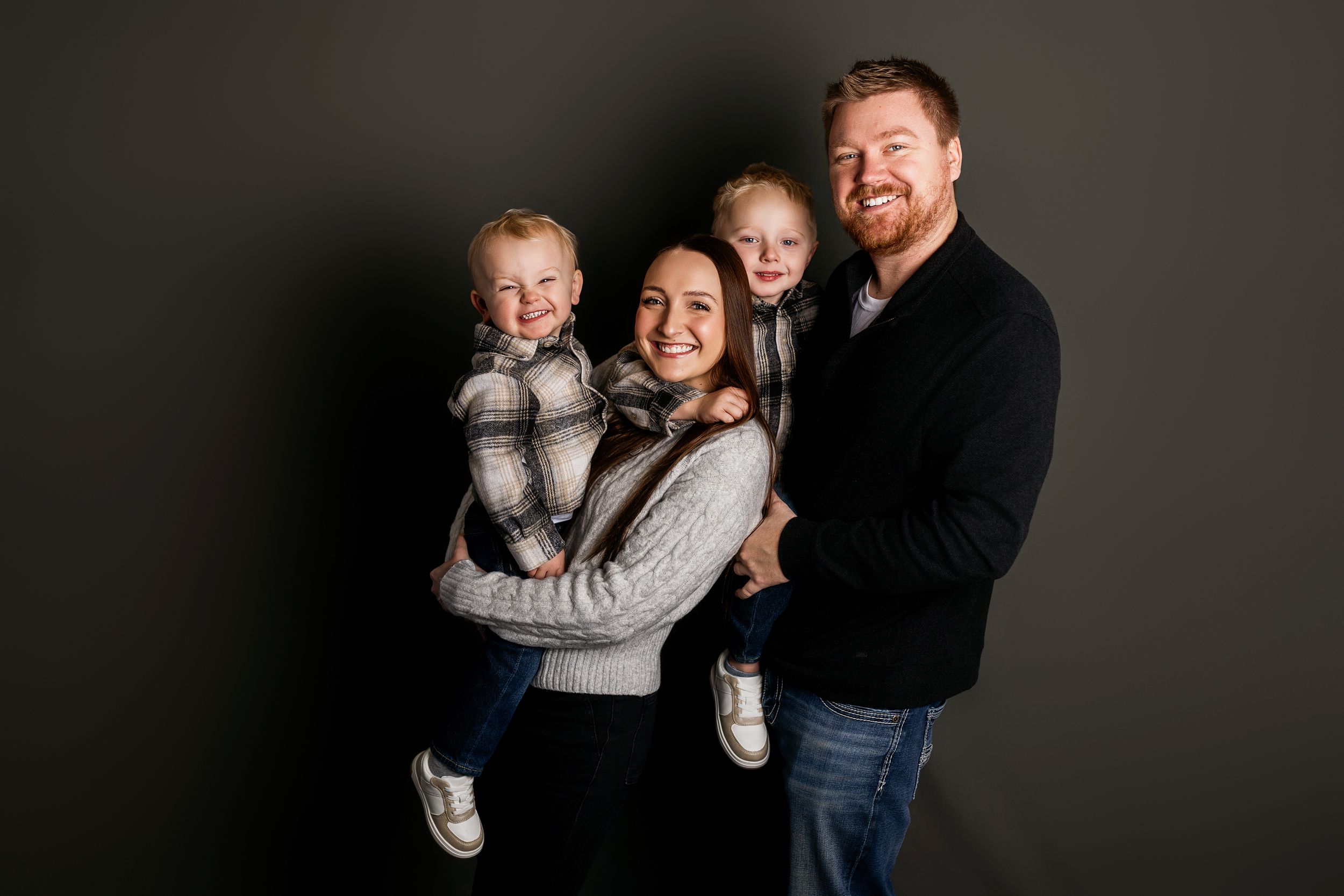 A happy family in casual attire poses together against a dark background for a series of candid portrait photos.