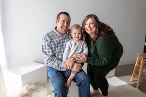 A family in coordinating outfits poses together for a series of casual indoor studio portraits against a white backdrop.