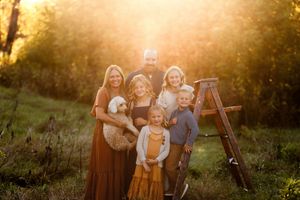 A group of people pose together in a golden field during sunset while wearing coordinating burgundy and cream outfits.