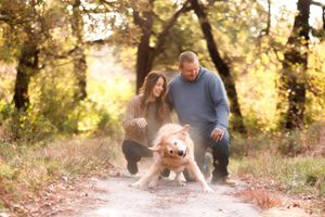 A couple walking their golden retriever on a sunlit forest trail during golden hour.