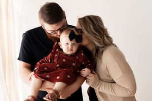 A family in coordinating outfits poses together against a white background for a portrait session.
