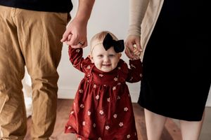 A child in a red floral dress stands with adults in casual attire against a neutral background.