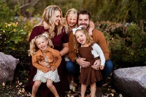A group of people laugh together while sitting outdoors during a family photo session in a natural setting.