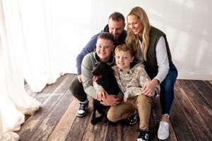 Family members share tender moments while sitting together on a dark wooden floor in a bright white room.