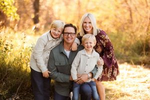 Family enjoying autumn outdoor photoshoot in a sun-drenched forest setting with golden foliage.