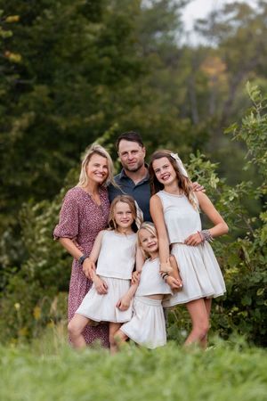 A family poses together outdoors in coordinated white outfits against a natural green background.