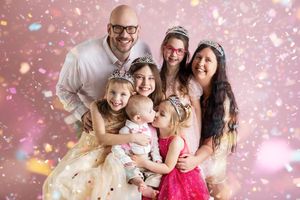 A group poses together against a pink sparkly backdrop with glittering confetti and bokeh effects.