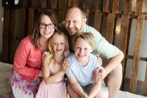 A smiling family poses together inside a rustic barn setting with wooden slat walls in the background.