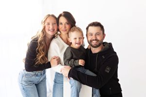 Joyful family of four posing together against white background in casual attire.