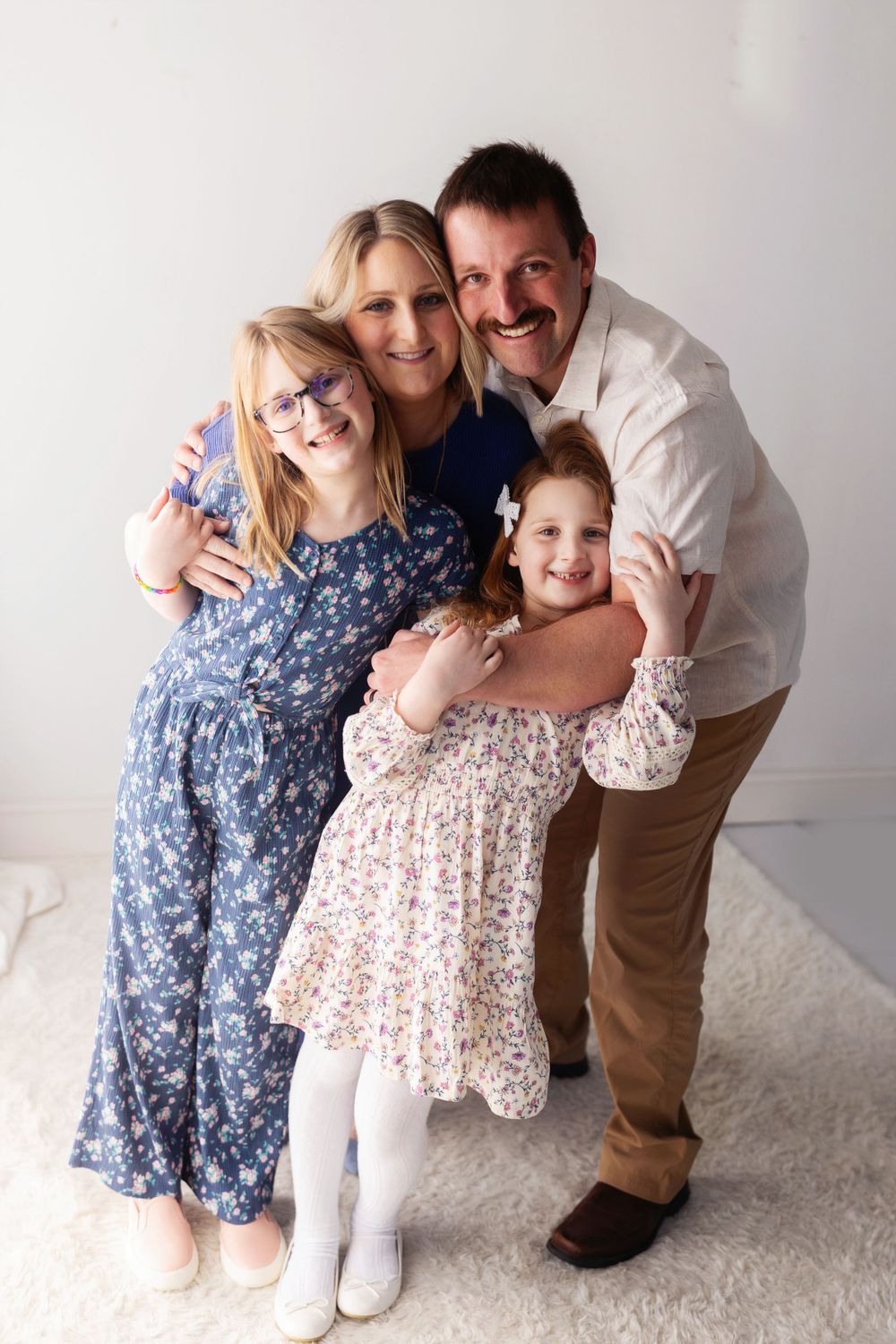 Heartwarming family poses together in coordinated floral outfits against a light background.