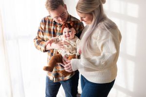 Happy family moment with parents holding their laughing baby in a sunlit room.