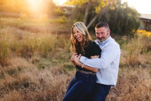 Couple embracing during golden hour sunset photo session in field.