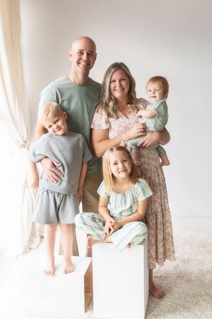 A family of five poses together for a portrait in soft neutral colors against a light background.