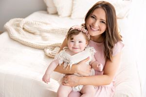 Mother and baby daughter share tender moment on white couch with knit blanket.
