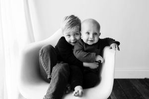 Black and white portrait of two children sharing a tender moment on white furniture.