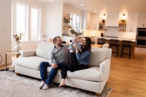 A couple relaxes and laughs together on a light gray couch in a modern open-concept living room.