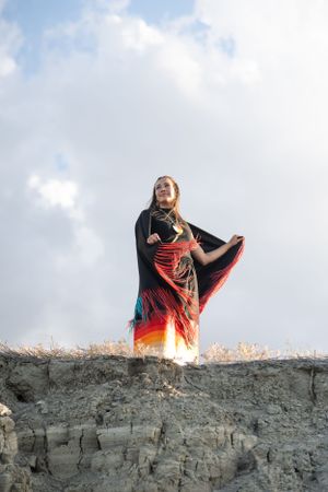 Dramatic silhouette of a high school senior wearing native attire  against a cloudy sky while standing on a rocky cliff.