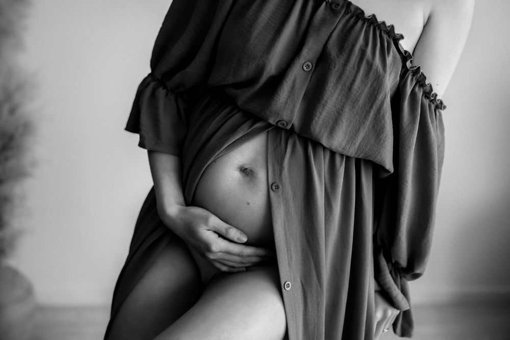 A black and white artistic maternity photo showing a pregnant belly beneath flowing fabric.