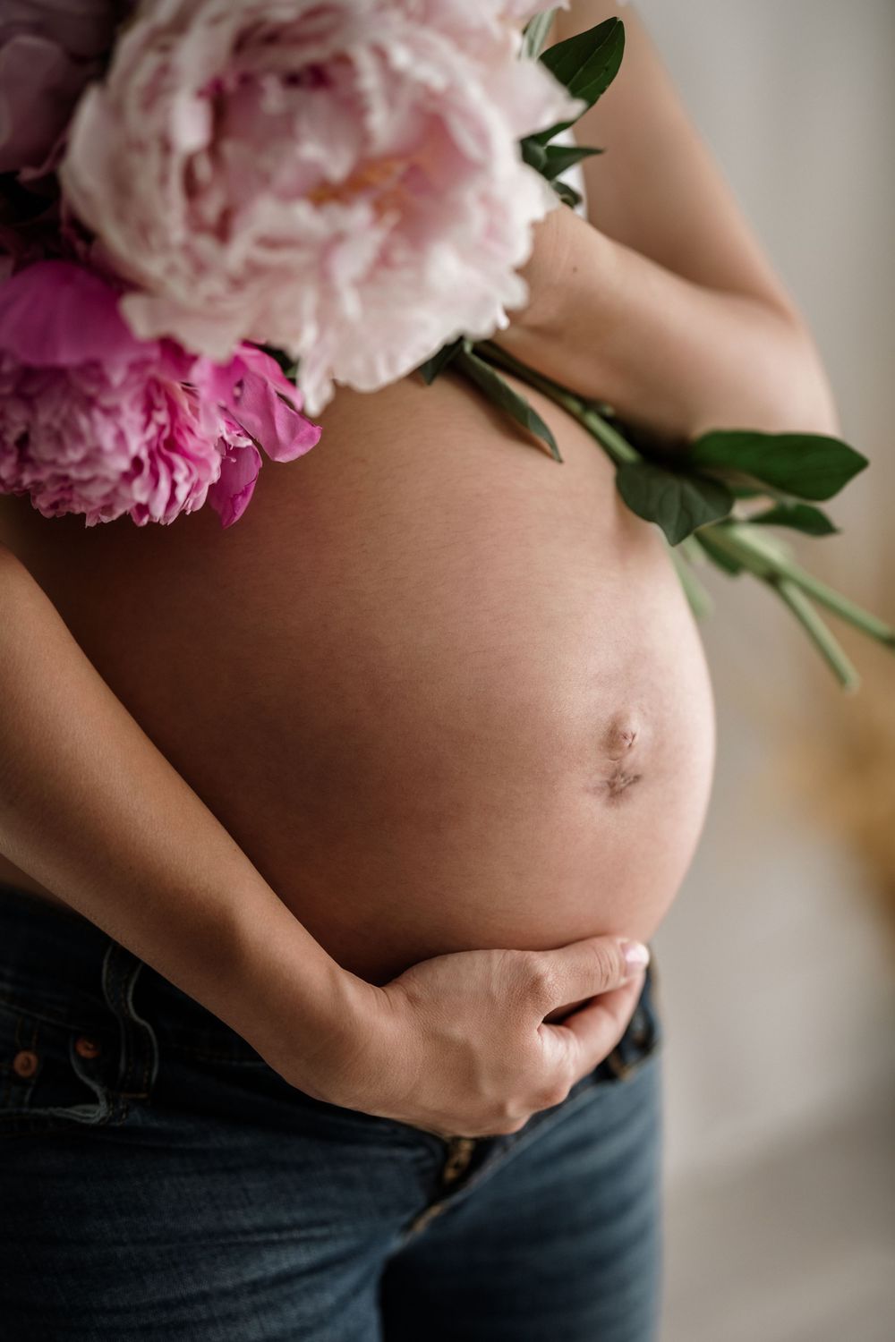 Close up of pregnant belly with pink peonies delicately placed against bare skin.