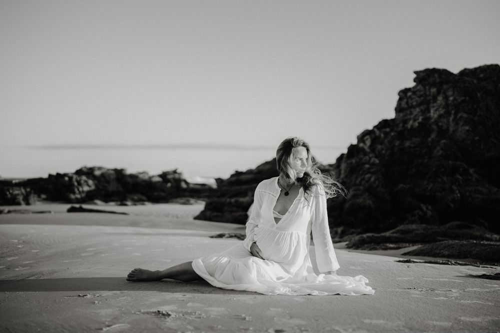 A black and white photo series shows a person in white clothing reclining on a beach with coastal rocks in the background.