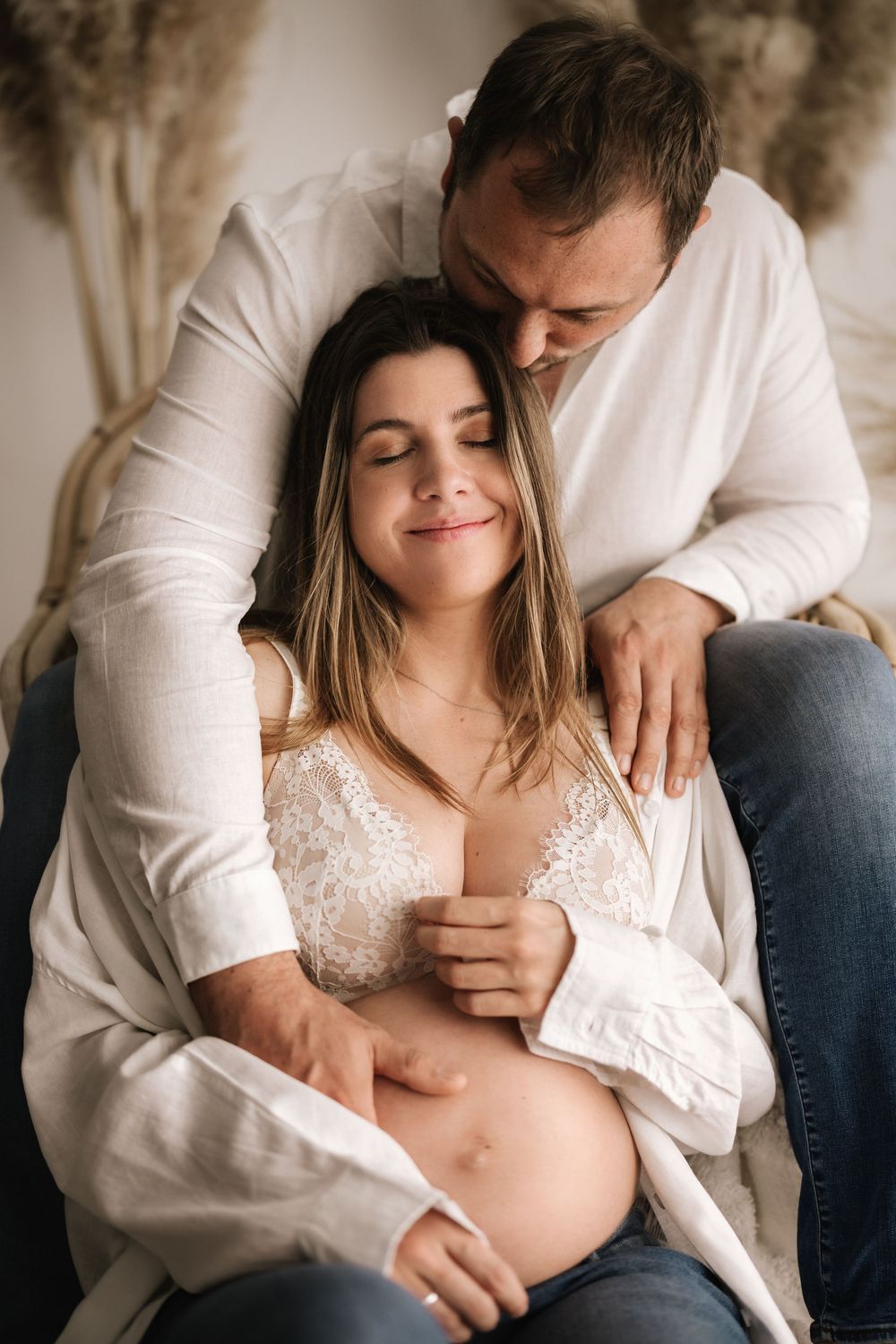 Intimate maternity photo of couple dressed in white embracing and sharing a tender moment.
