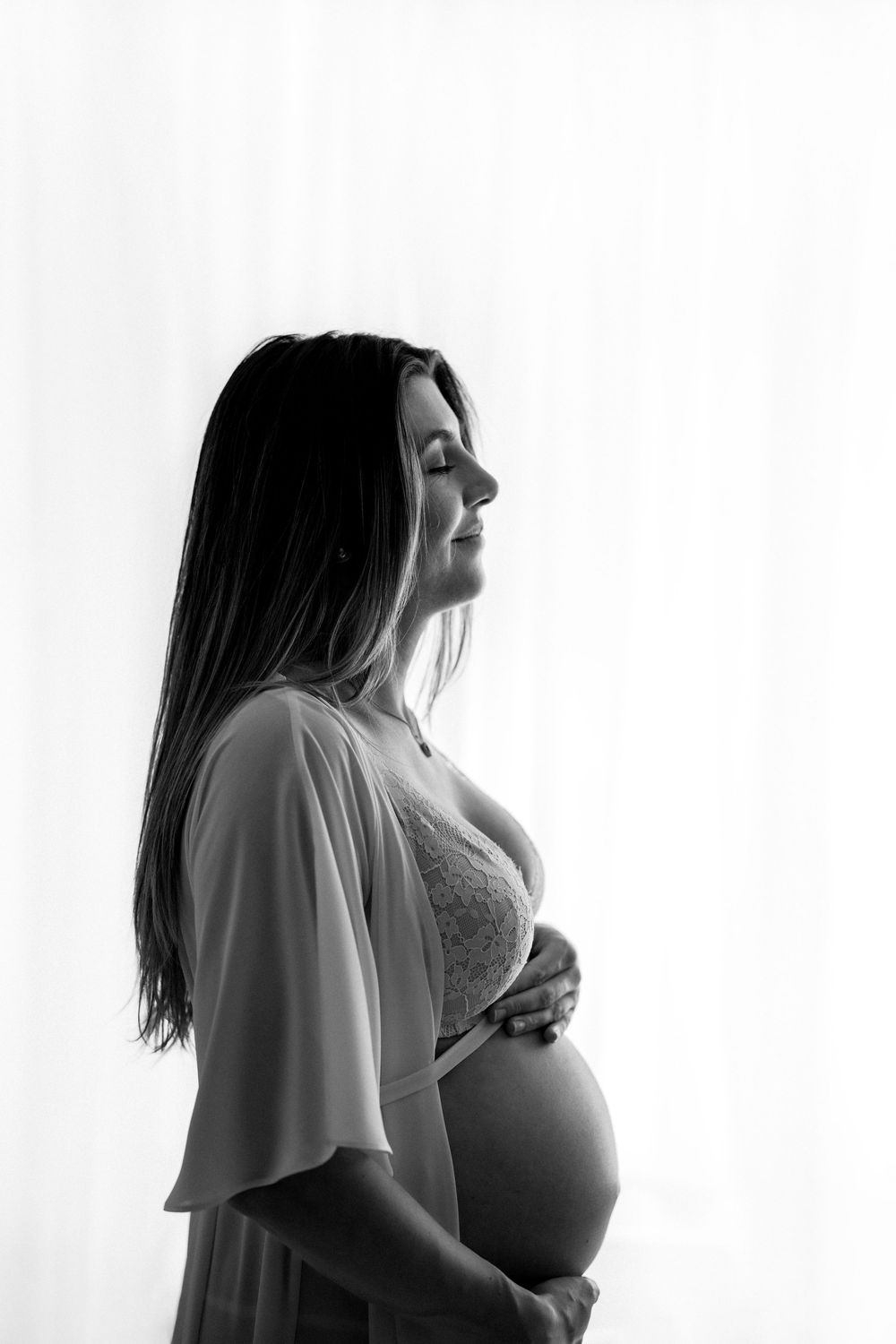 Black and white silhouette of an expectant mother in a flowy dress showing her pregnant profile against a light background.