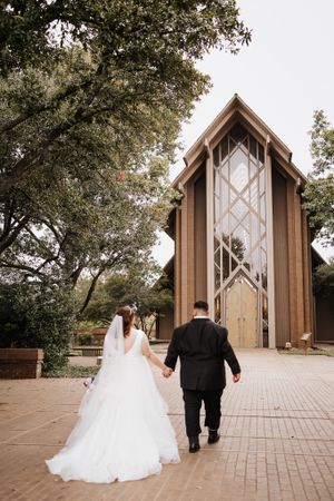 Couple walks toward modern chapel with dramatic architectural details.